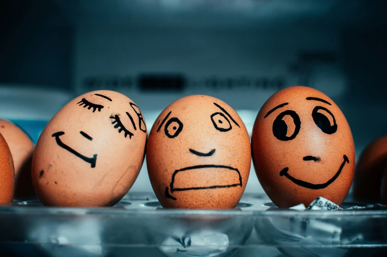 six eggs with drawn faces standing together in an egg bowl