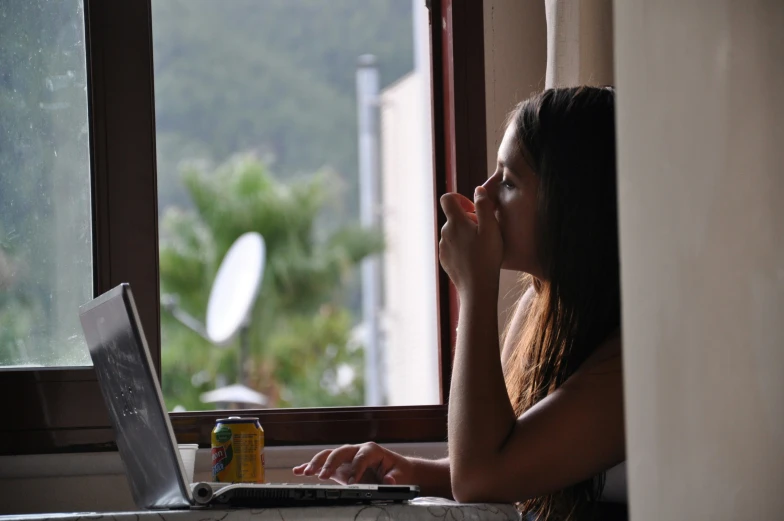 a woman sits at her laptop in front of a window