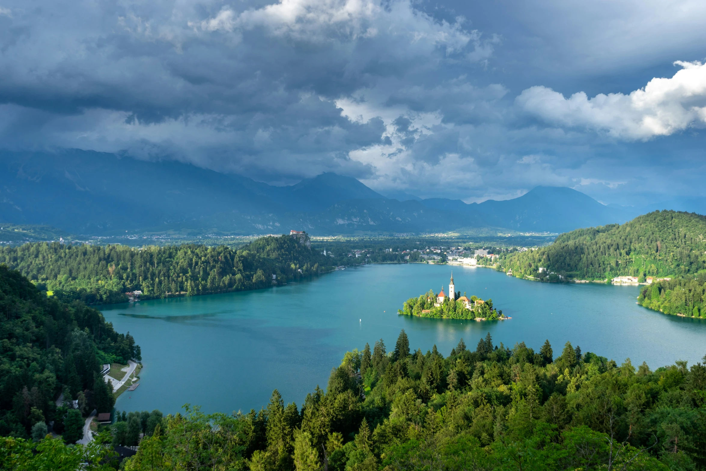 a lake surrounded by trees and mountains under a cloudy sky