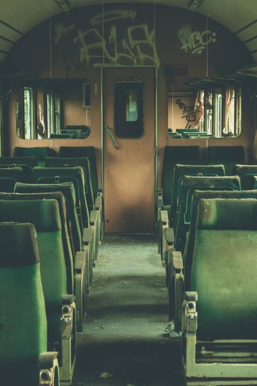 an empty and dilapidated train car has green seats and graffiti on the walls