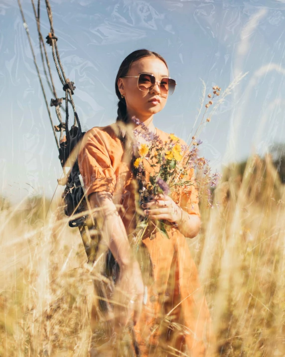 a woman in an orange dress holding a rifle stands next to dry grass