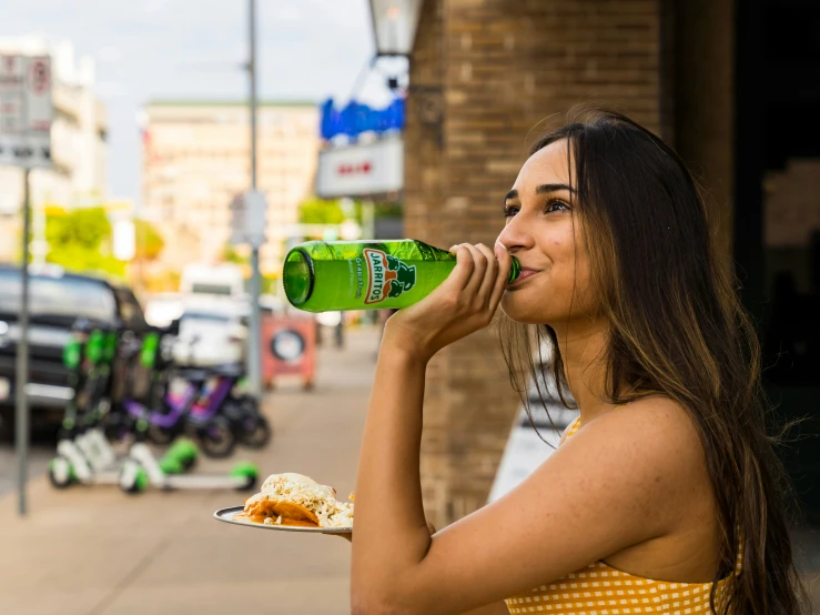 a woman in yellow drinking from a green bottle