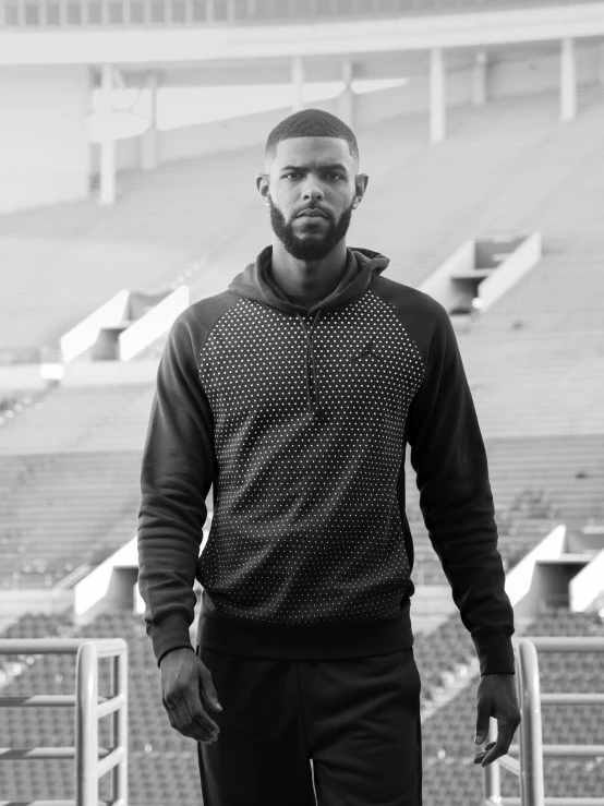 a male with a beard in a sweatshirt standing near the bleachers