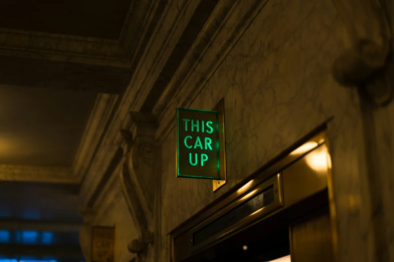 a green sign that reads this car up hangs on the side of a building