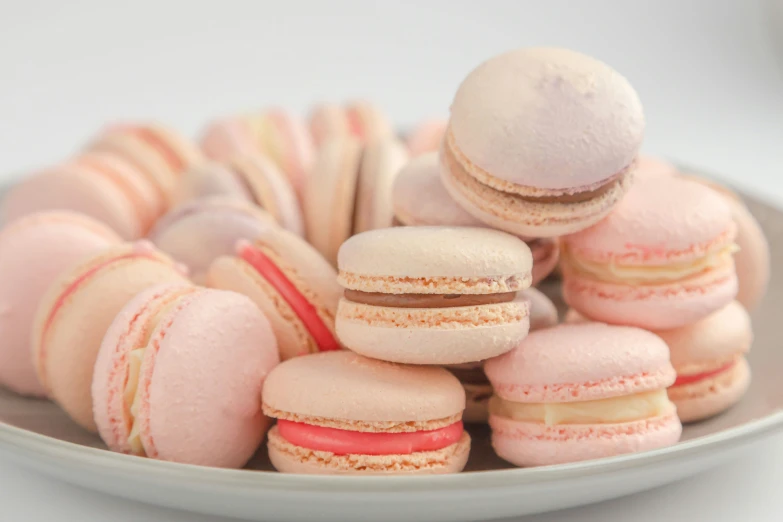 several pink and yellow macarons sit on a white plate