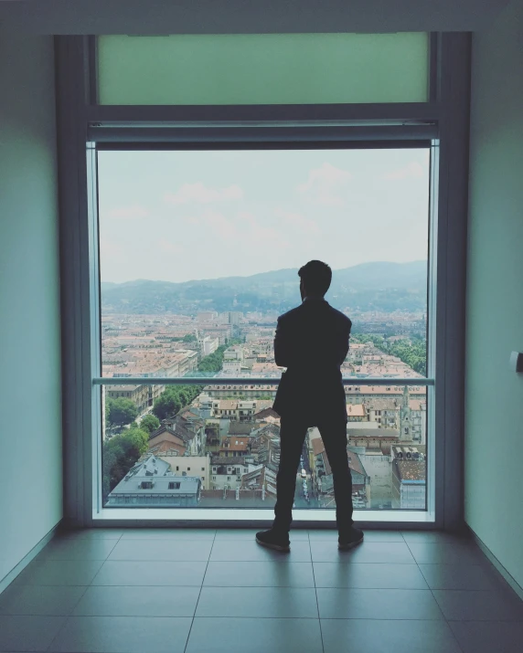 a man standing in front of a window looking out at the city