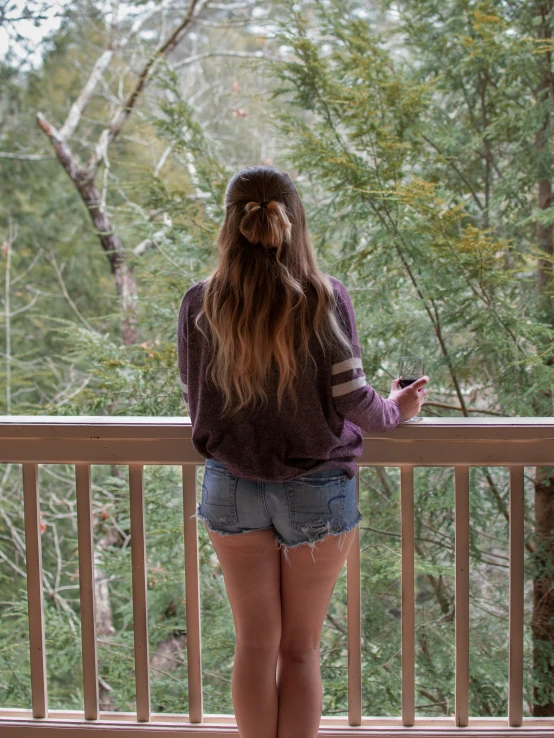 a woman on her cell phone at a balcony overlooking the woods