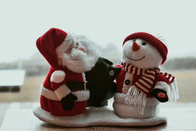 two toy snowmen in winter clothing on a surface