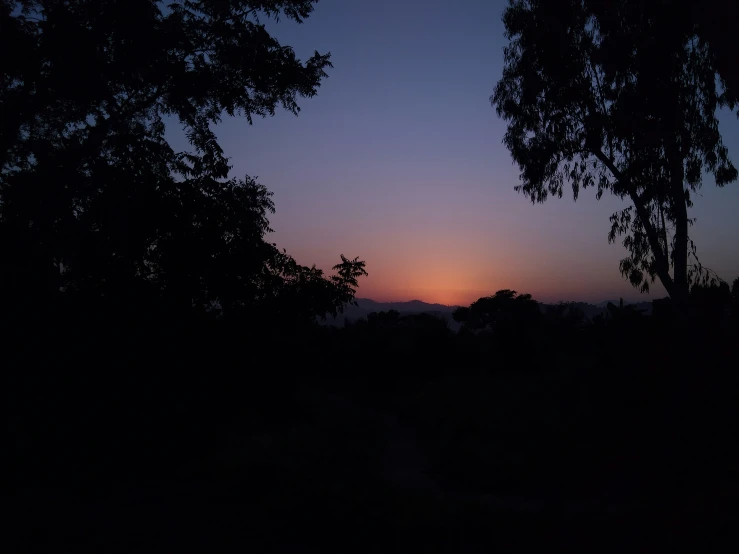 the sun is setting over the mountain through the trees