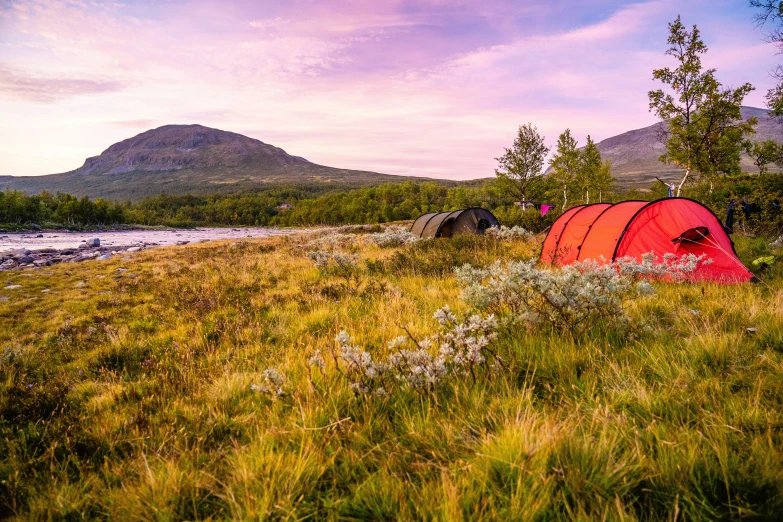 red tent in grassy field with lake in background