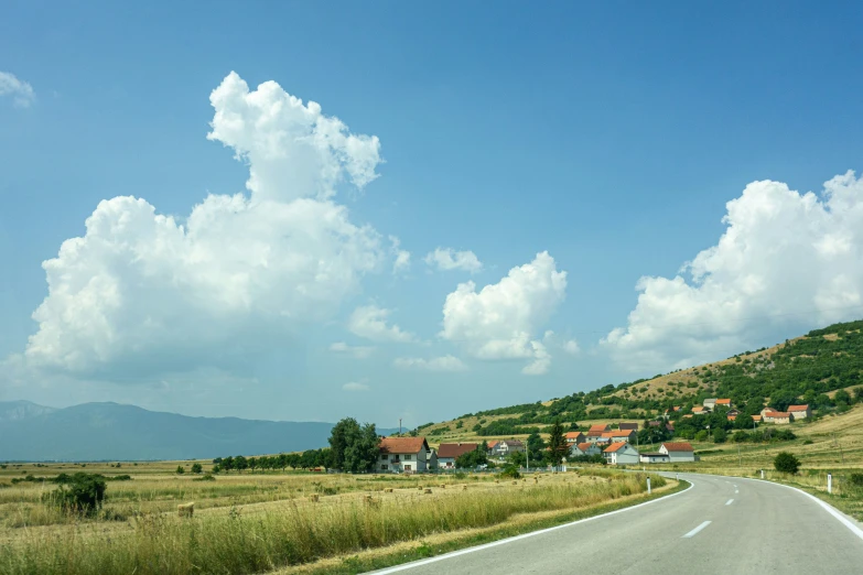 a long rural road is next to a grassy hill