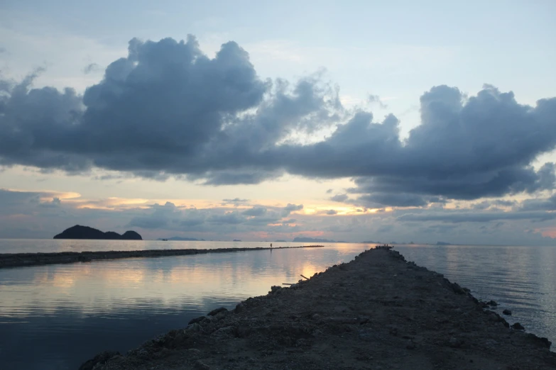 an empty breakwater and small island under clouds