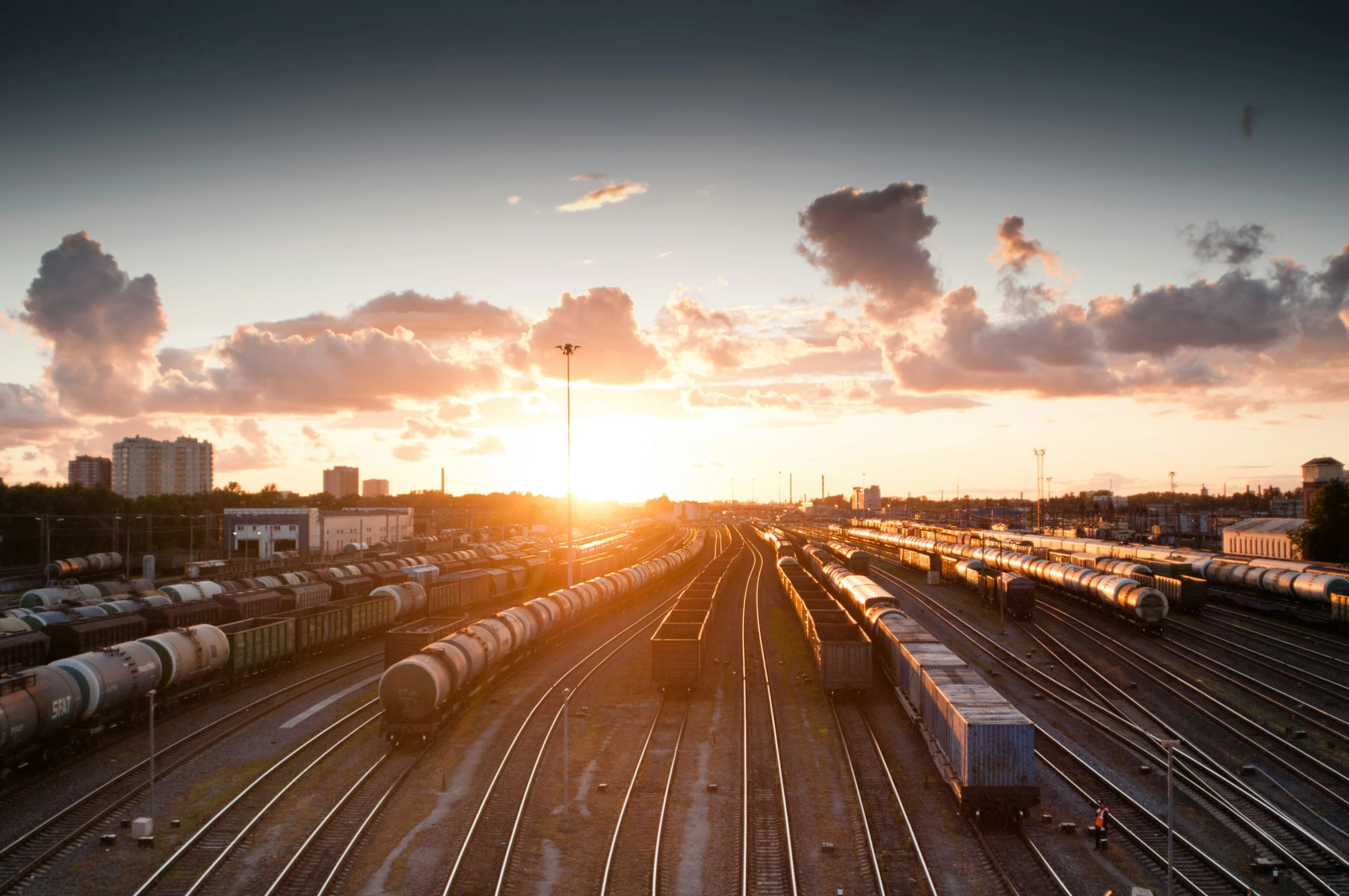 train tracks with many trains near the sun in the sky