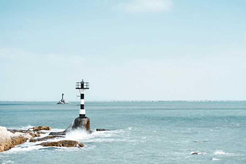 a lighthouse at the beach, next to rocks and water