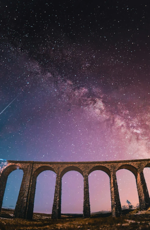 the stars and galaxy are above an old brick bridge