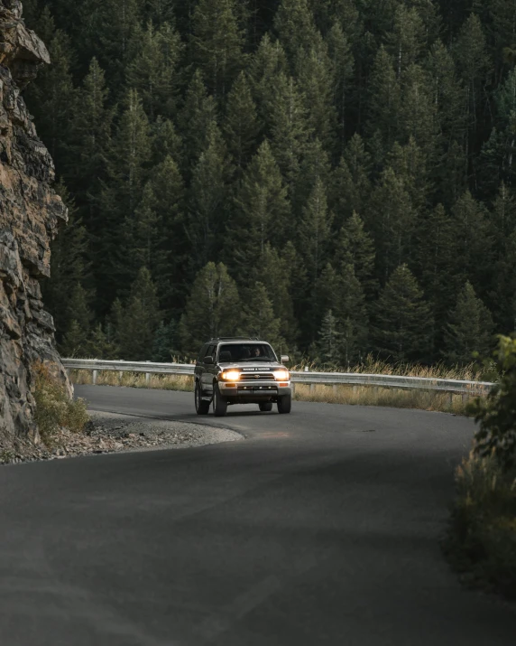 a truck driving down a road by a large rock wall