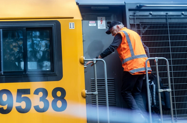 man in safety vest opens the door to a train