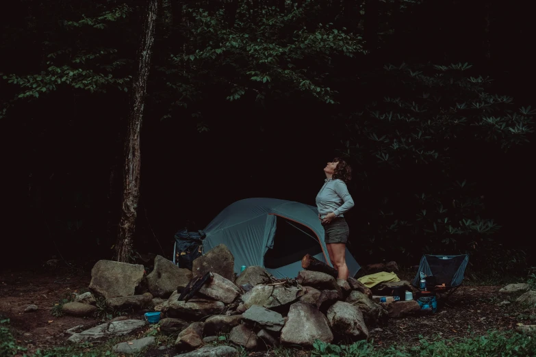 woman standing in the middle of some rocks near a tent