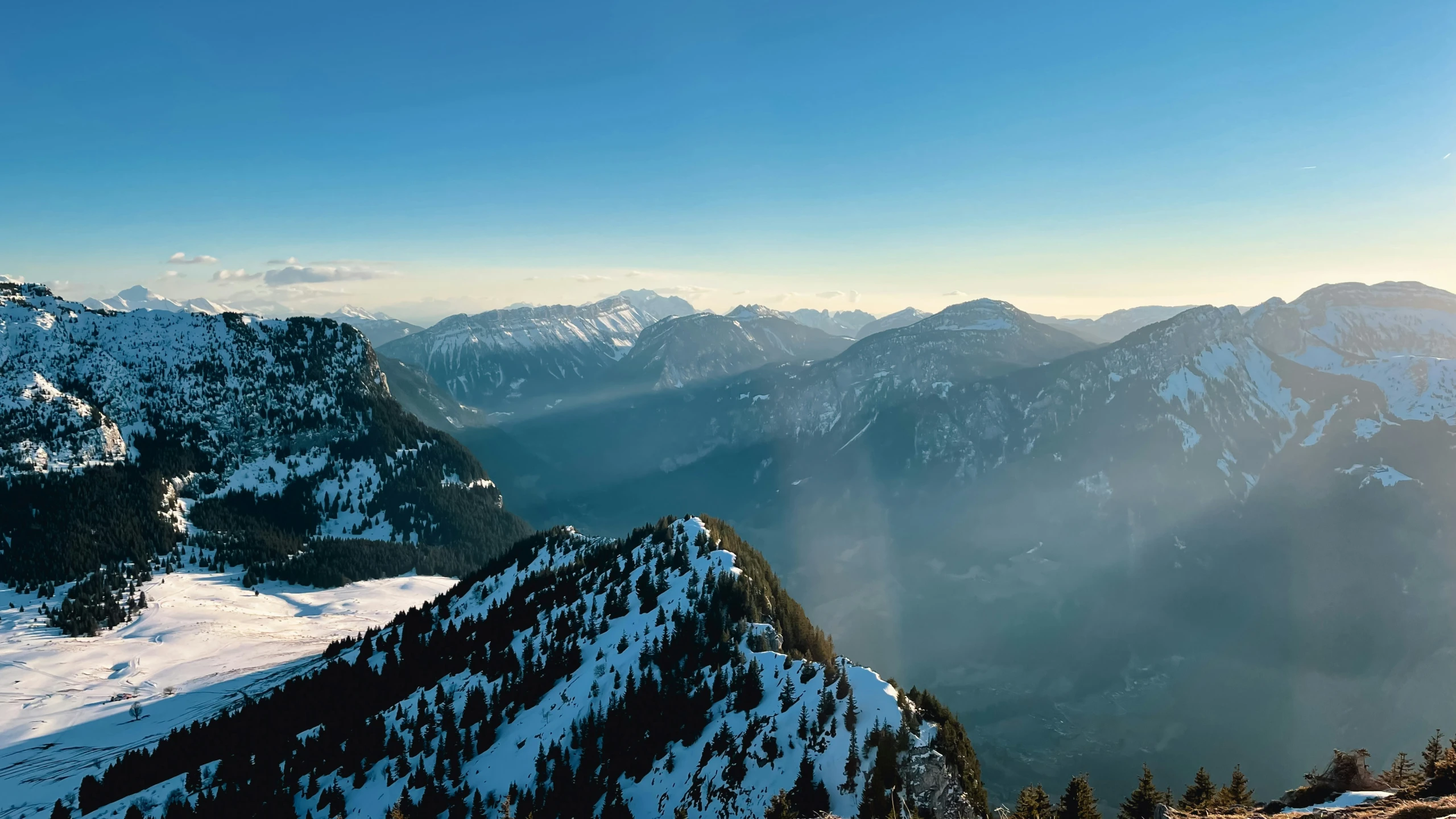 some mountains and snow covered trees and a person standing at the top