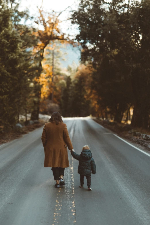 a woman walking down a road holding hands with a child