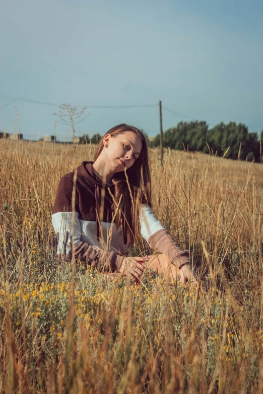 a young woman sitting in a field in a brown shirt