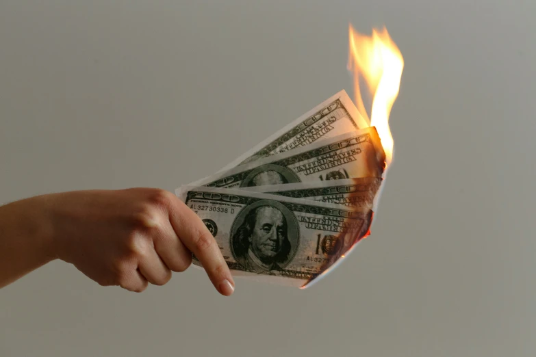 a burning dollar bill and hand on fire