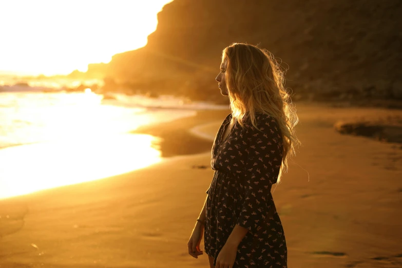 a young woman standing on a beach during the sunset