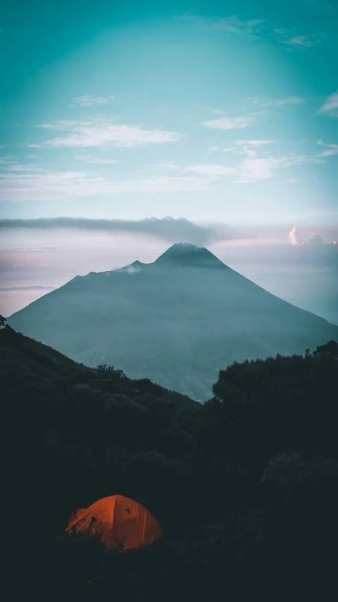 a tent pitched on the ground at dusk overlooking a mountain