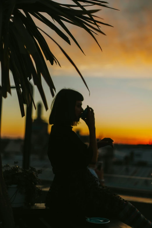 a woman sitting at the edge of a building drinking from a bottle