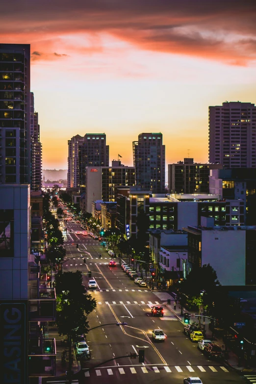 a sunset in the middle of a street with tall buildings