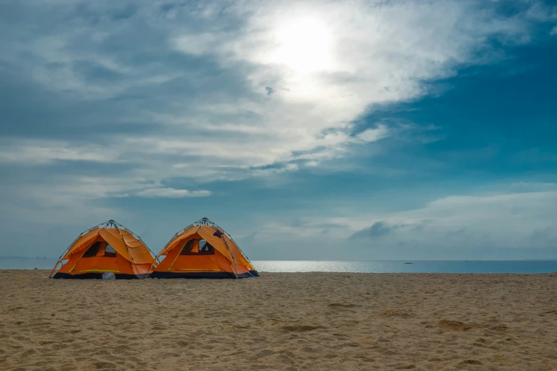 two tents sit on the beach in front of the ocean