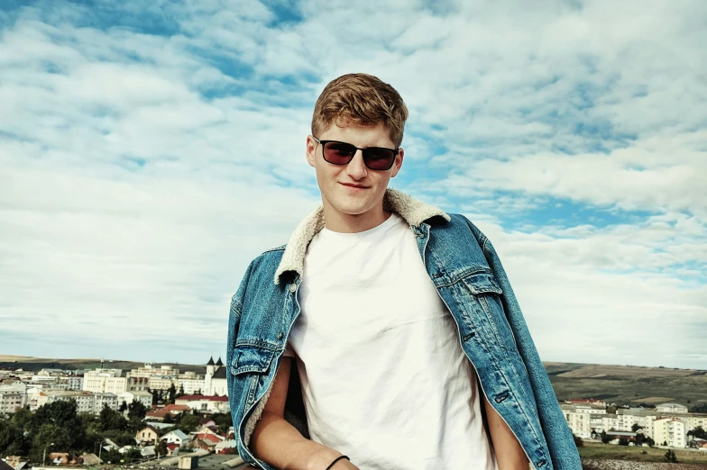 a man in a blue jean jacket and sunglasses stands in the city