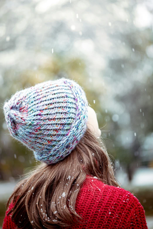 a  with her back turned up, is wearing a hat that is knitted and has colorful yarn