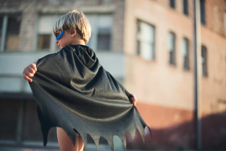 a small child wearing a cape standing on the sidewalk