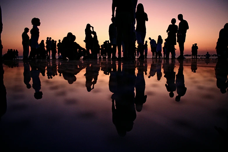 people stand on the beach at sunset with their reflection in the water