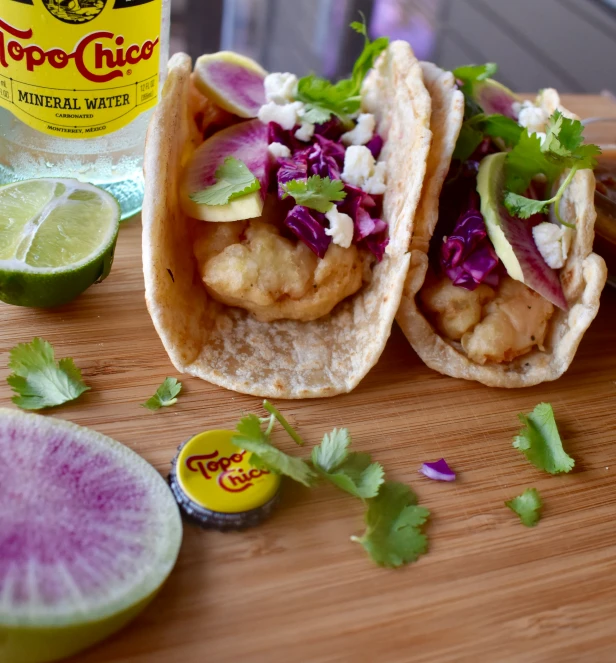 two chicken tacos with cabbage, coleslaw, limes and a can of pop century cilantro
