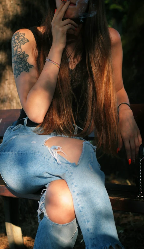 a woman with tattoos smoking a cigarette on a bench