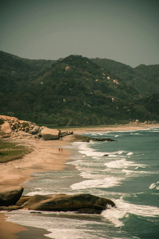 a po taken from a hill shows a rocky beach and mountain range in the distance