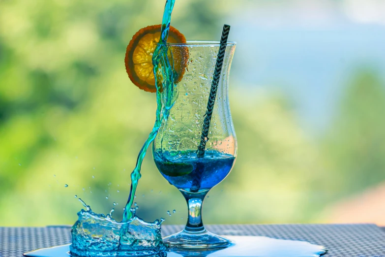 water splashes into a blue liquid in a tall glass