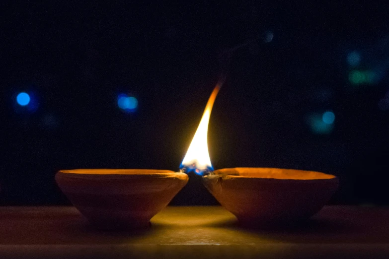 a close up of two small bowls with a lit candle in the middle of them