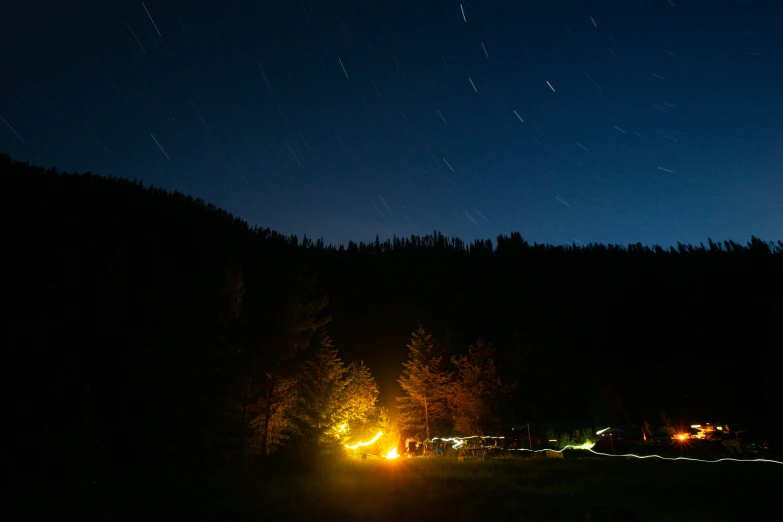 the night sky above the tree tops shows the bright lights of cars and a mountain