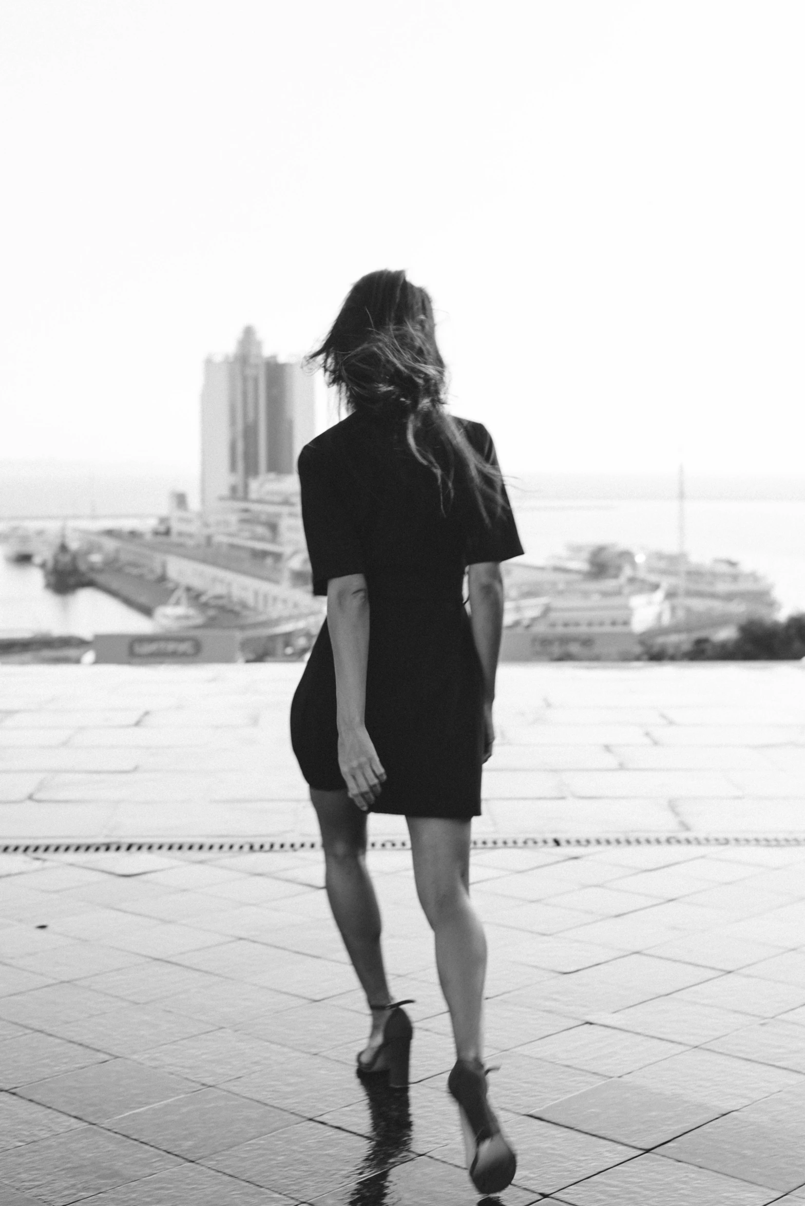 woman in black dress and high heels walking away from the ocean