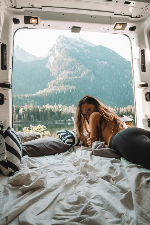 a beautiful young woman laying in bed next to an open van window