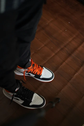 a person's feet and sneakers with orange laces