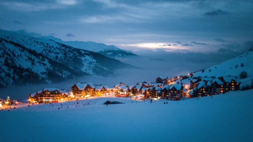 a snow covered ski slope with lit up buildings