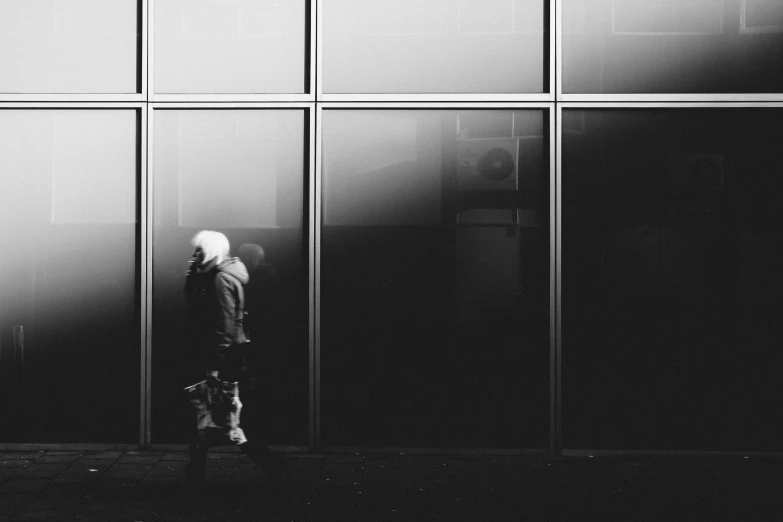 black and white pograph of person walking in front of a building