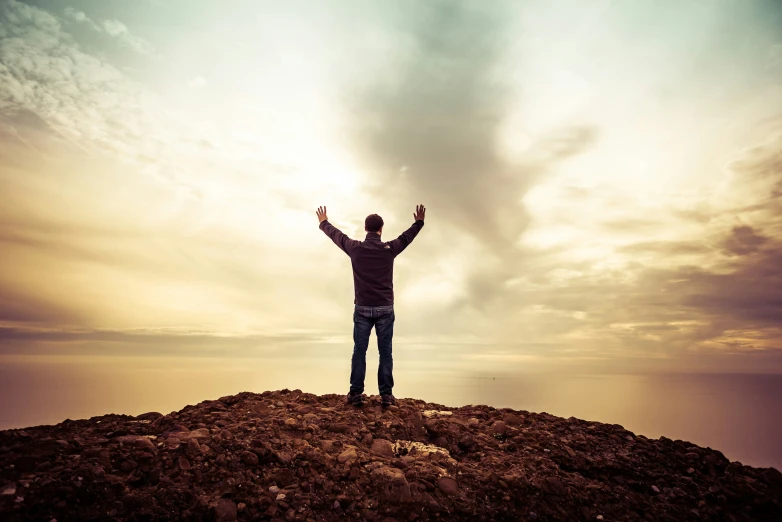 a person stands on top of a rocky hill with their arms raised