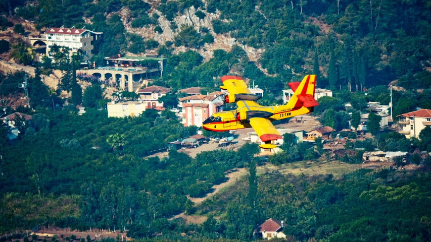 a yellow and red airplane flying above a lush green hillside