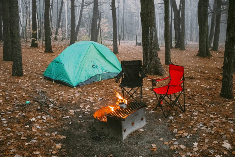 two chairs next to a fire in the woods