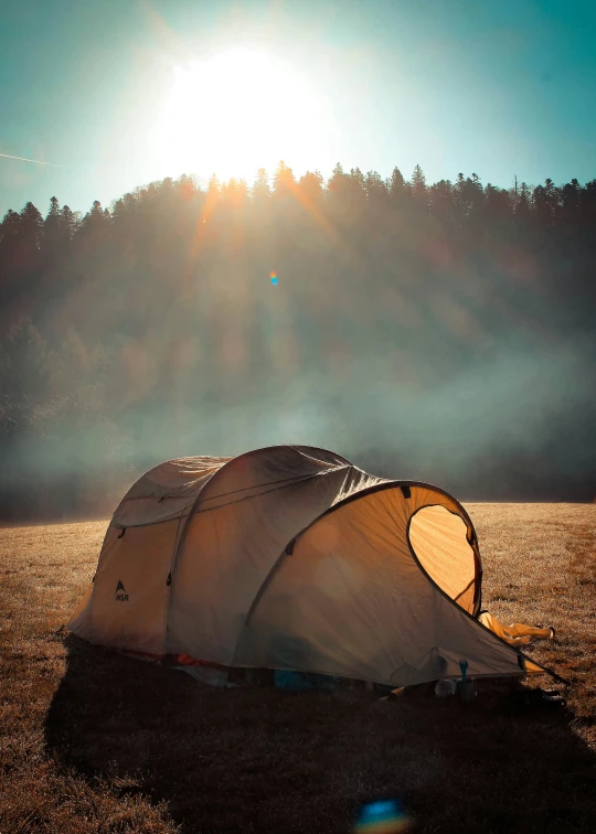 a tent sitting on top of a field in front of the sun